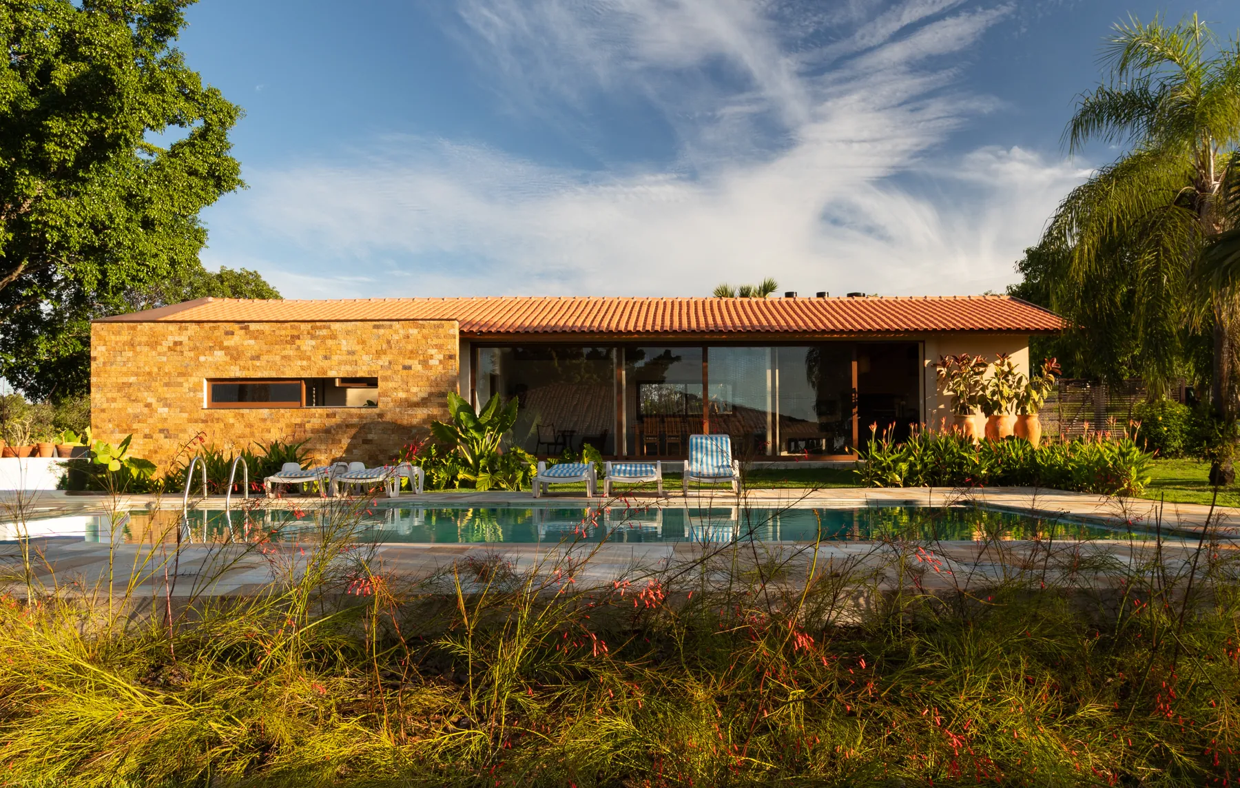 Residência com piscina envolvida por jardim tropical no fim de tarde, projeto do Estúdio Natu