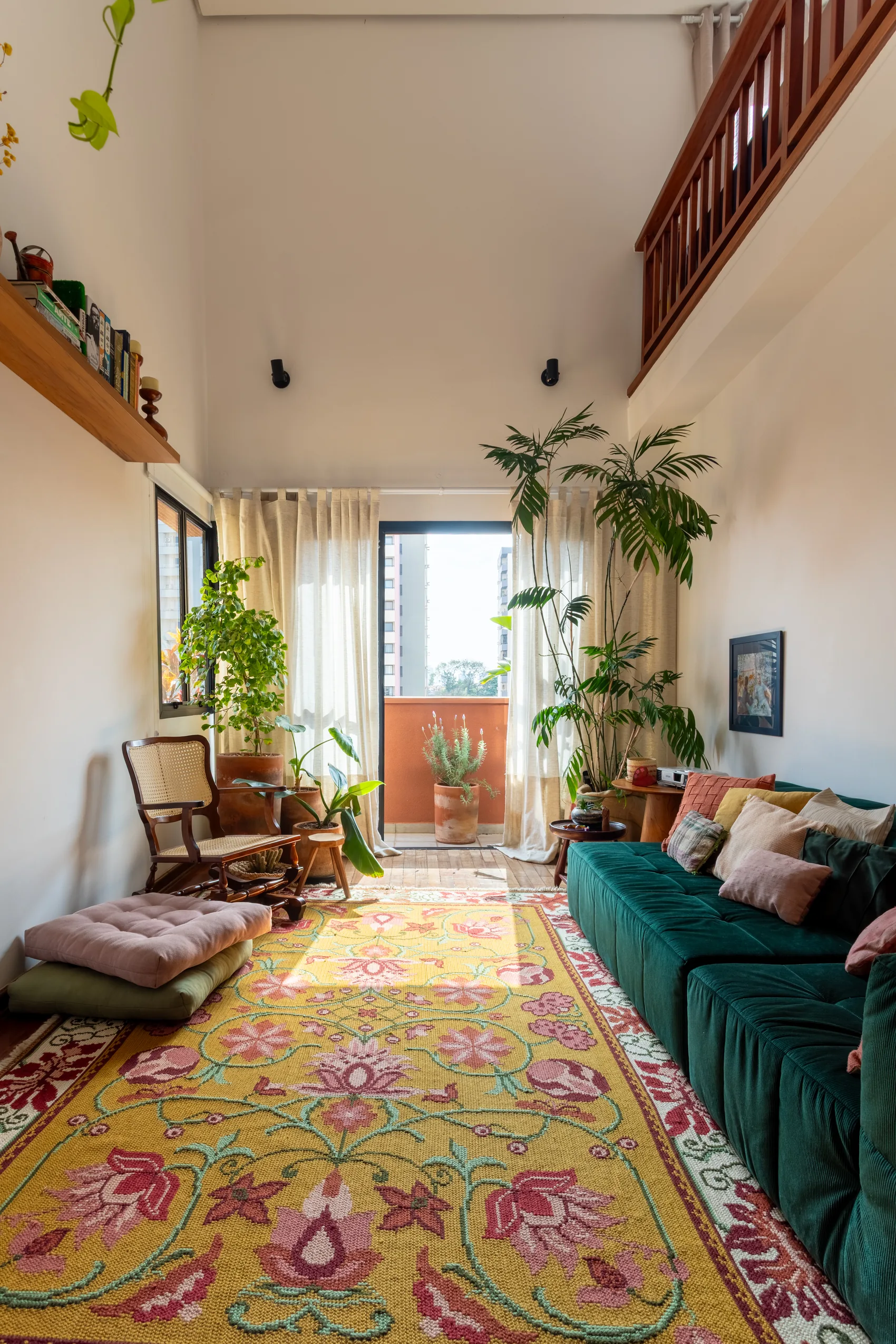 Sala de estar com sofá verde, tapete floral e plantas junto à varanda