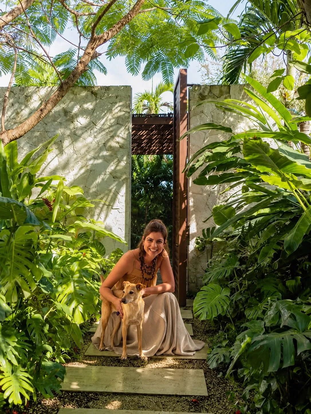 Thaísa Sampaio sorrindo em meio a um jardim de monsteras e palmeiras